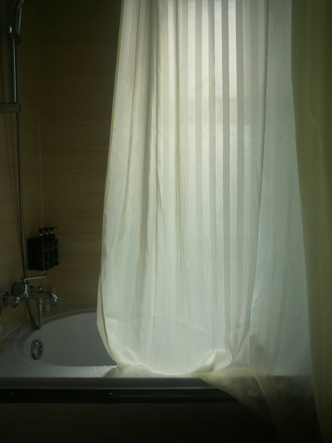 A white striped shower curtain drawn across a bathtub, with a shower hose and taps on the left.
