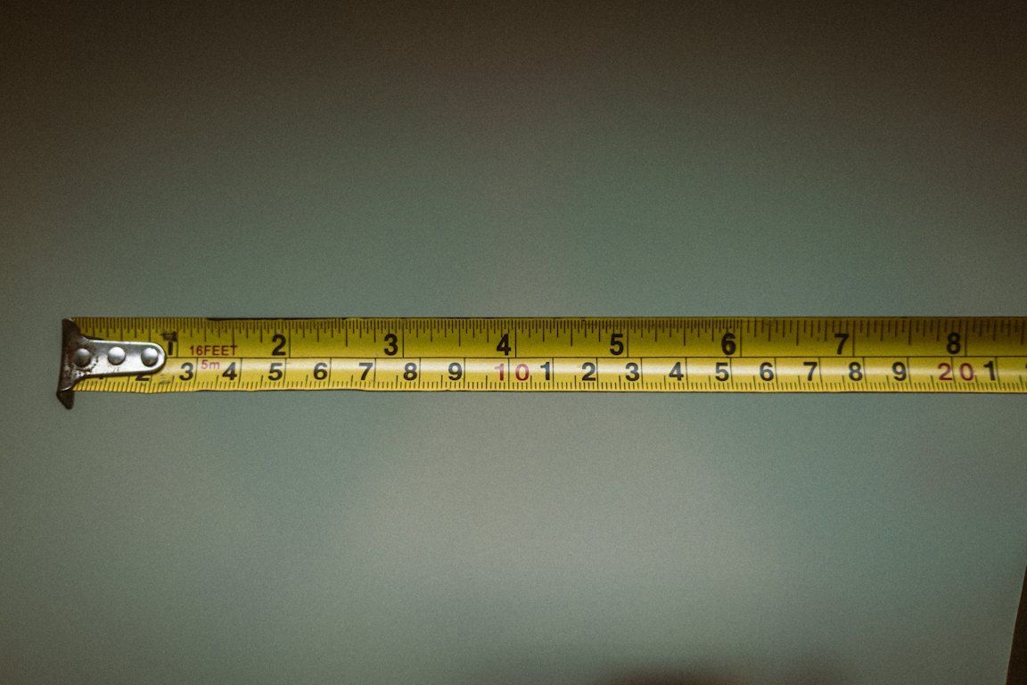 A yellow tape measure pulled out horizontally against a grey-green background.