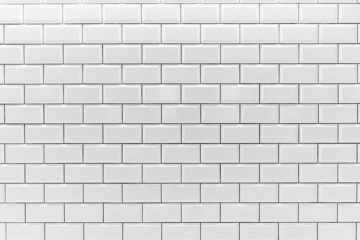 A wall completely covered with white rectangular tiles with bevelled edges, laid in a staggered pattern and separated by thin dark grout lines.